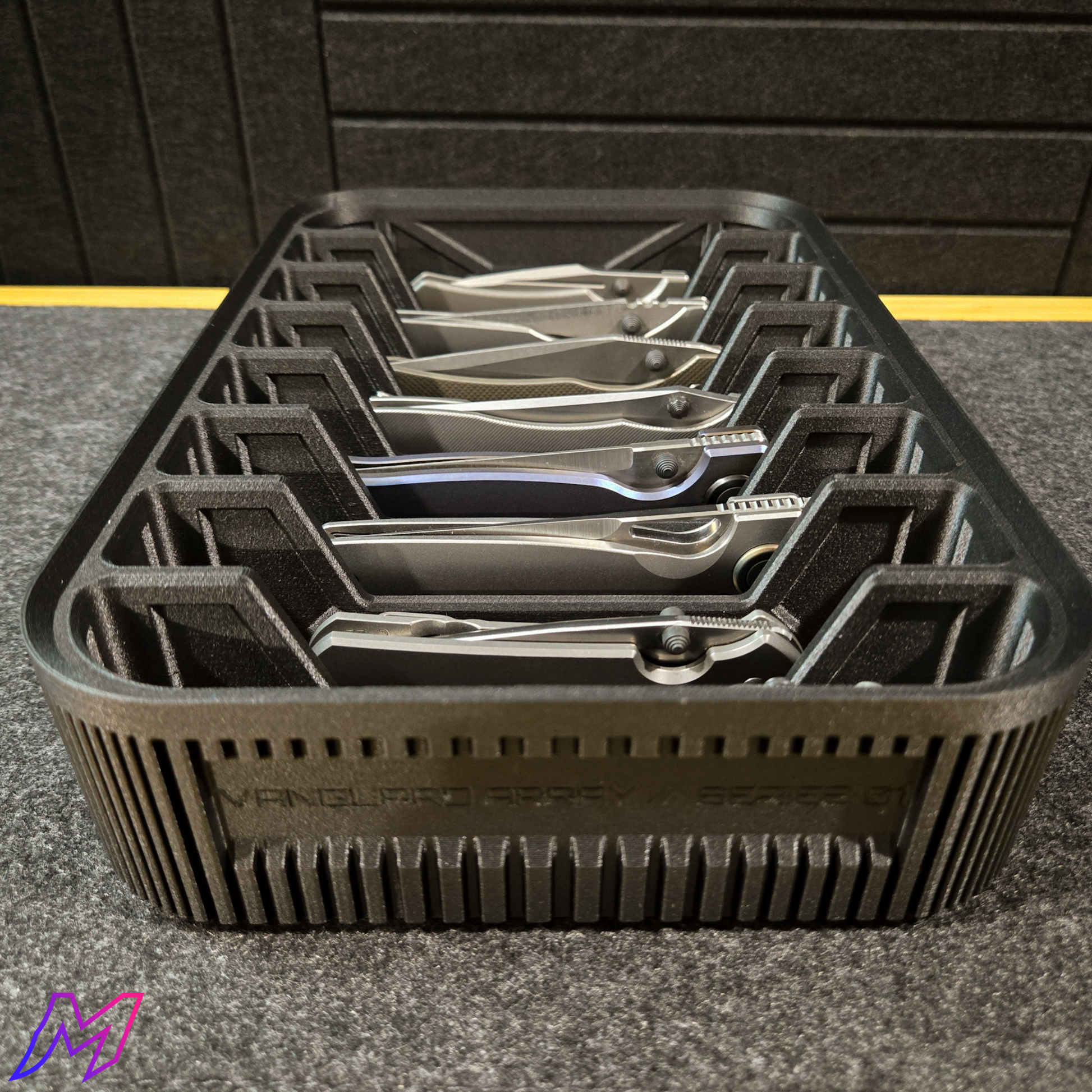 MATERIUM Vanguard Array low-angle view with folding knives loaded, amber base visible through ribbed slots