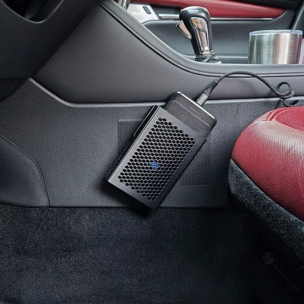 MATERIUM universal top-load phone holder mounted on car console side panel, phone seated in holder with charging cable, red interior