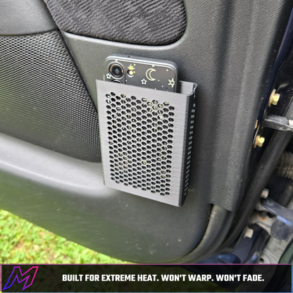 MATERIUM universal phone holder mounted on door panel outdoors, phone loaded, fuchsia bar reads Built for Extreme Heat Won't Warp Won't Fade