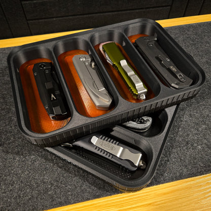 MATERIUM Vanguard Catch Stealth colorway hero shot, loaded with 4 EDC folding knives and accessories on amber base